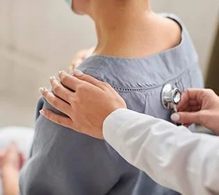 Médica auscultando as costas de uma paciente com estetoscópio